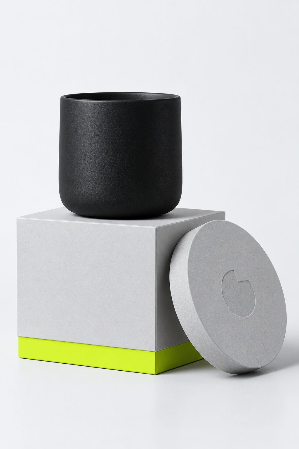 A graphite stoneware cup on its pale grey box, the lid leaning beside it with a debossed notched circle